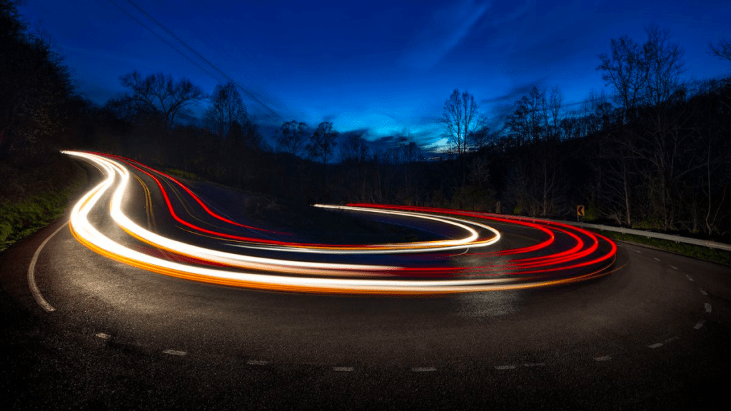 long exposure of cars going around a turn at night 